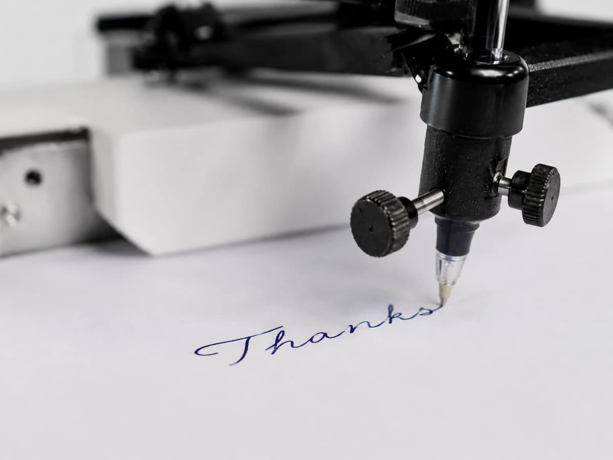 A handwriting machine using a ballpoint pen to write the word Thanks in blue ink